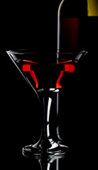 A glass of red wine and a bottle on a black background.