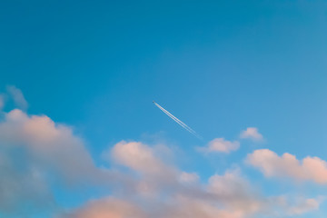 Blue sky with pink clouds and airplane trail. Nature background