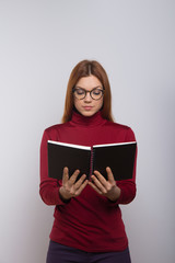 Focused female college student reading book. Serious young woman in eyeglasses holding notebook and looking down isolated on white background. Education concept