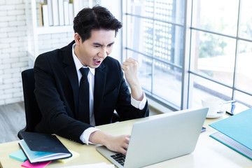 Fototapeta premium Happy of asian young businessman see a successful business plan on the laptop computer and pen on wooden table background in office,business expressed confidence embolden