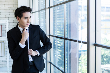 Portrait of a cheerful mature asian young businessman wear a business suit of man in blue jacket and blue shirt looking at the window In the office room background.