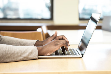 Female black student working on computer in classroom. Hands of young woman sitting at desk and...