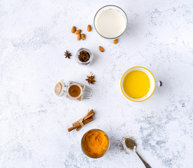 Vegan turmeric latte in a mug, almond milk, spices on white textured background, top view