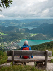 Fototapeta na wymiar Woman with backpack sitting on wooden bench under tree in mountains enjoying scenic view