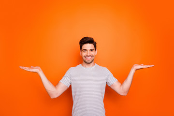 Photo of funny attractive guy hold open palms hands advertising two new popular products low prices shopping wear striped t-shirt isolated bright orange color background