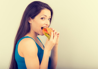 Thinking funny hungry excited woman eating burger and looking down on blue background.