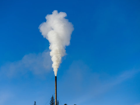 White smoke comes out of a black chimney in the blue sky. Ecology theme