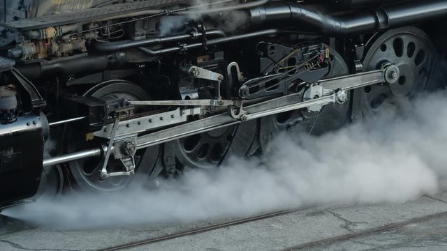 Panning shot of piston, connecting rods, coupling rods and drive wheels of train as it departs station.