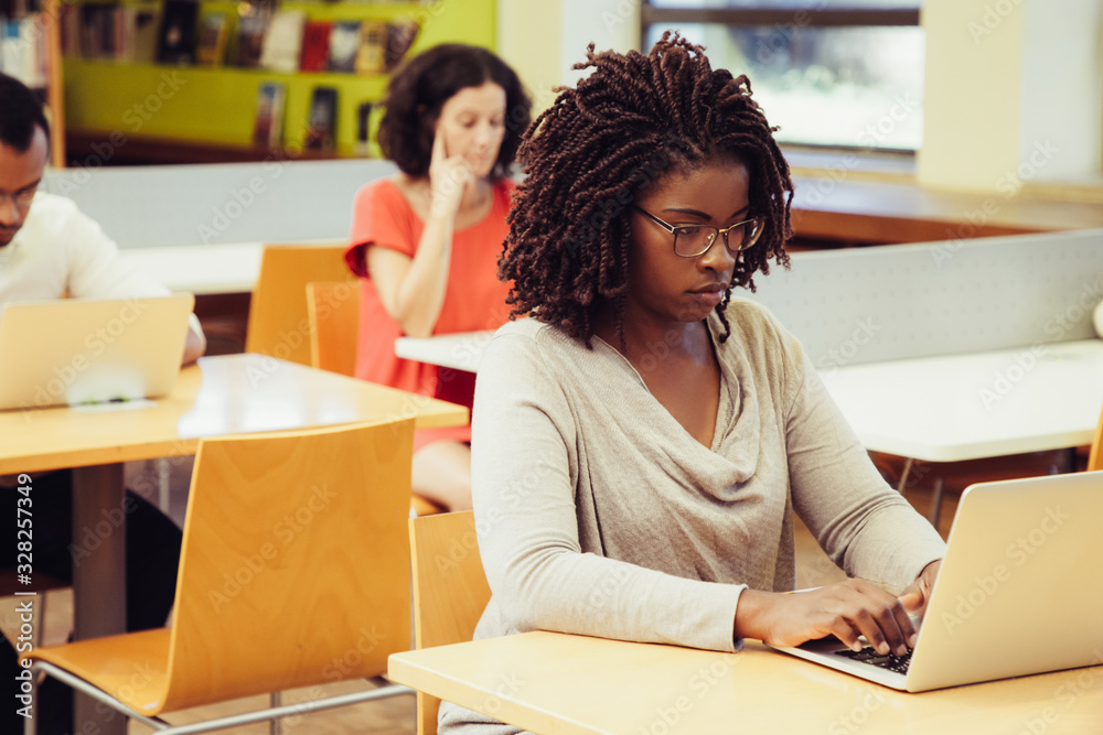 Wall mural multiethnic adult students working on computers in public library. people sitting at desks and using