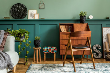 Modern and retro composition of home office interior with wooden cabinet, chair, plants, decoration and elegant personal accessories. Stylish vintage concept of home decor. Wood panelling. Template.