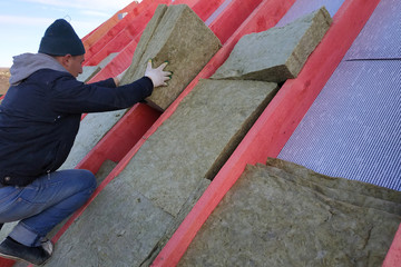 The worker puts mineral wool on the roof, insulating the house.