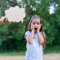 Pretty surprised thinking little girl posing summer nature outdoor with cloud of thoughts (like in comic book). Kid's portrait. Emotions, feeling and thoughts of child