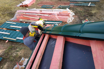 The worker installs and attaches a metal tile to the roof of the house.