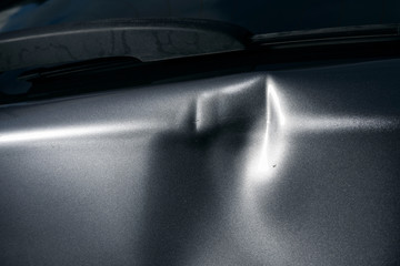 A dent in the body of a silver car