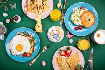 Easter composition with breakfast flat lay with scrambled eggs bagels, tulips, pancakes, bread toast with fried egg and green asparagus, colored quail eggs. Top view.