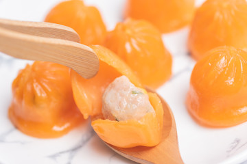 A bun like an orange in a white plate on the table