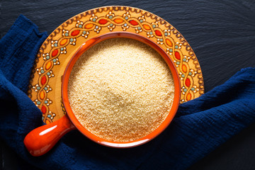 Food concept organic raw couscous in orange bowl on blask slate stone board with copy space © TYSB
