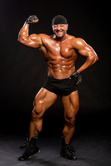 Handsome muscular bodybuilder in black shorts and bandana posing in studio