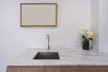 Modern faucet and wash basin sink on white marble counter with wooden photo frame space for advertising, yellow orchid flower
