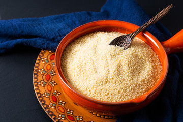 Food concept organic raw couscous in orange bowl on blask slate stone board with copy space © TYSB