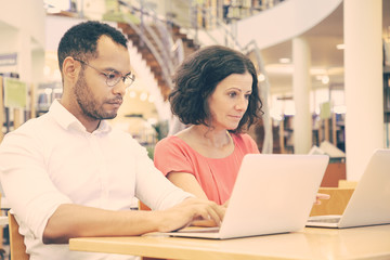 Focused college students working in library computer class. Man and woman in casual sitting at desk, using laptops, typing. Education concept