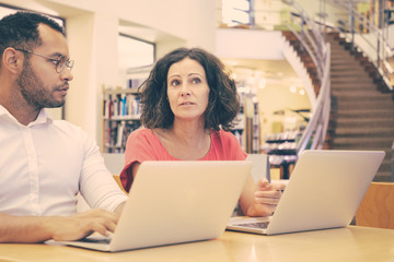 Excited college students discussing research specifics in library. Man and woman in casual sitting...
