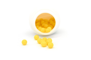 Fototapeta na wymiar yellow round tablets lie in a white jar and are scattered around it isolated on white background