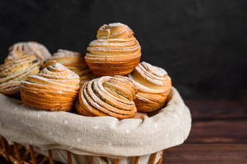 Delicious modern cruffins are made from layered croissants in the shape of a muffin. cruffins with a wooden basket on a dark background, sprinkled with powdered sugar.