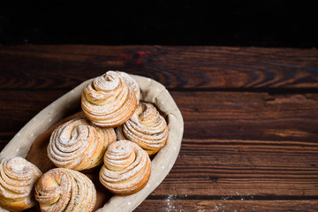 Delicious modern cruffins are made from puff croissants in the form of a muffin. cruffins with a wooden basket on a dark wooden background, sprinkled with powdered sugar and raspberries. Copy space