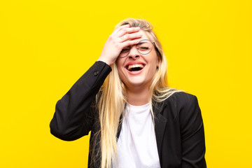 young pretty blonde woman laughing and slapping forehead like saying d‚Äôoh! I forgot or that...