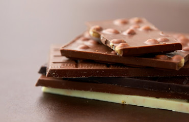 sweets, confectionery and food concept - bars of dark, white and milk chocolate with nuts on brown background