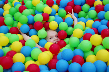 Fototapeta na wymiar The child hid in balls in the pool with many colored balls in the children's playroom.