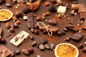 sweets, confectionery and culinary concept - cocoa beans, chocolate, nuts and cinnamon sticks on brown background