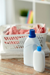laundry, wash and housekeeping concept - baby clothes in basket with detergent and conditioner bottles on wooden table at home