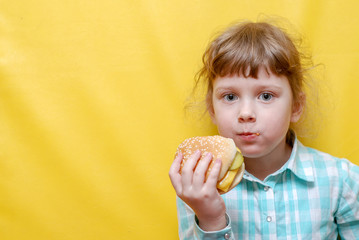 Beautiful little girl eating a hamburger. Yellow background. Fast food, restaurant meal.