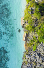 View from above, stunning aerial view of some bungalows surrounded by rocky cliffs bathed by a turquoise, crystal clear sea. Malwawey Coral Garden, Coron Island, Palawan, Philippines.