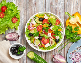 Greek salad with cucumeber, olives, feta cheese, cherry tomatoes, bell pepper, onion and lettuce. Diet, vitamin food. Healthy vegetarian meal concept. Tasty salad in bowl on wood, flat lay.