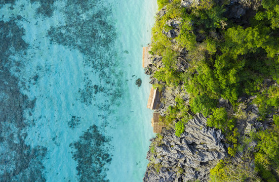 View from above, stunning aerial view of some bungalows surrounded by rocky cliffs bathed by a turquoise, crystal clear sea. Malwawey Coral Garden, Coron Island, Palawan, Philippines. © Travel Wild