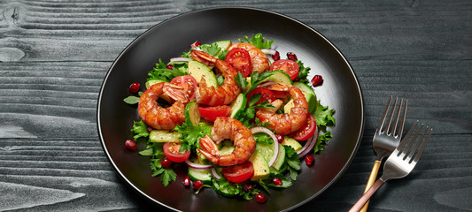 Shrimps salad, avocado, lettuce, cherry tomatoes. Home made vegetarian shrimp salad. Seafood concept. Tasty veg mixed leaves, grilled prawn shrimps in plate on black wood background.