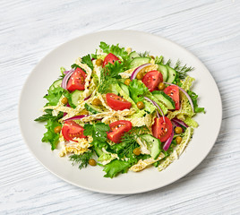 Fresh salad with cherry tomatoes, savoy cabbage, cucumeber on dish. Healthy summer salad vegetarian meal concept. Tasty mixed leaves, tomatoes and mix vegetable salad on white wood