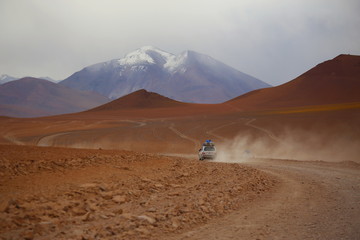 Bolivia desert in Potosi province, Andes highlands. Off road vehicle 4x4 crossing the arid land in the desert. Wild scenery with arid  soil, mountains and cloudy sky. Off road adventure.