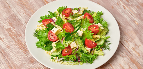 Fresh salad with cherry tomatoes, savoy cabbage, cucumeber on dish. Healthy summer salad vegetarian meal concept. Tasty mixed leaves, tomatoes and mix vegetable salad on wood background