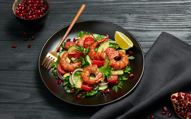 Shrimps salad, avocado, lettuce, cherry tomatoes. Home made vegetarian shrimp salad. Seafood concept. Tasty veg mixed leaves, grilled prawn shrimps in plate on black wood background.