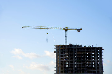 Tower crane constructing a new residential building at a construction site against blue sky. Renovation program, development, concept of the buildings industry.
