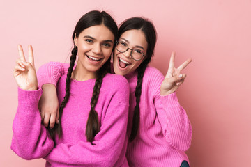 Image of two happy teenage girls smiling and gesturing peace fingers - obrazy, fototapety, plakaty