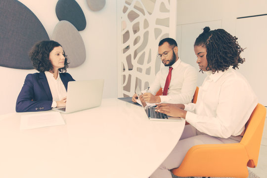 Diverse business colleagues reporting to female boss. Business man and women using laptops, checking documents and talking. Corporate meeting or leadership concept