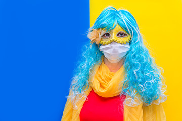 Concept of protection against coronavirus at carnival venice. A bright woman in a blue wig and yellow carnival mask, wearing a medical health mask from Virus crown celebrating the holiday. Copy space