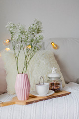 Spring home cozy interior. A bouquet of flowers in a vase, a cup of tea, decor on the sofa.