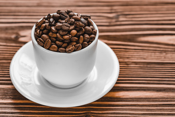 full white cup with coffee beans with plate on brown wooden background