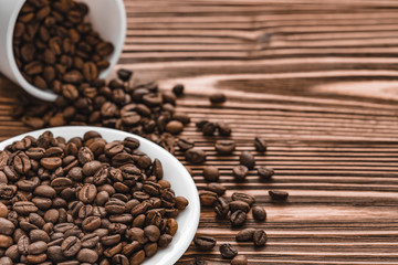 white plate and cup of coffee beans on brown wooden background. scattered grains around the saucer